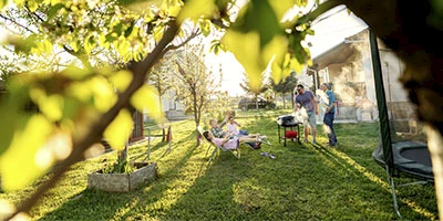 Weitläufiger Garten mit Bäumen und einer Familie am grillen und entspannen